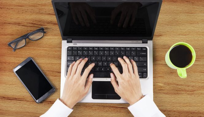 Hands working on table with laptop computer, smartphone, and coffee